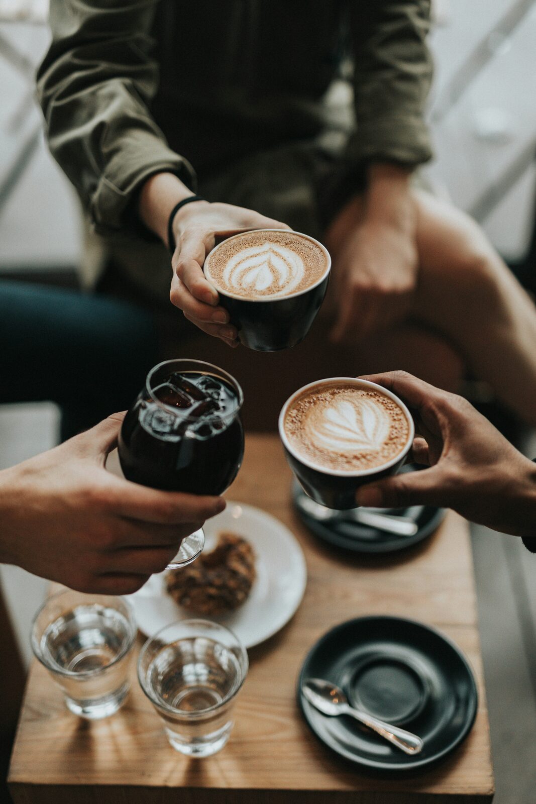 Friends raising three cups of coffee around a café table