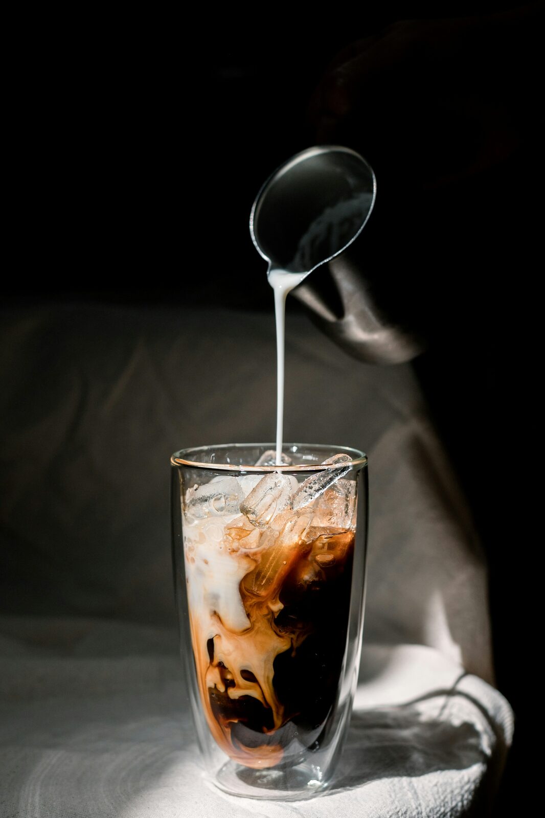 Milk being poured into a glass of iced coffee