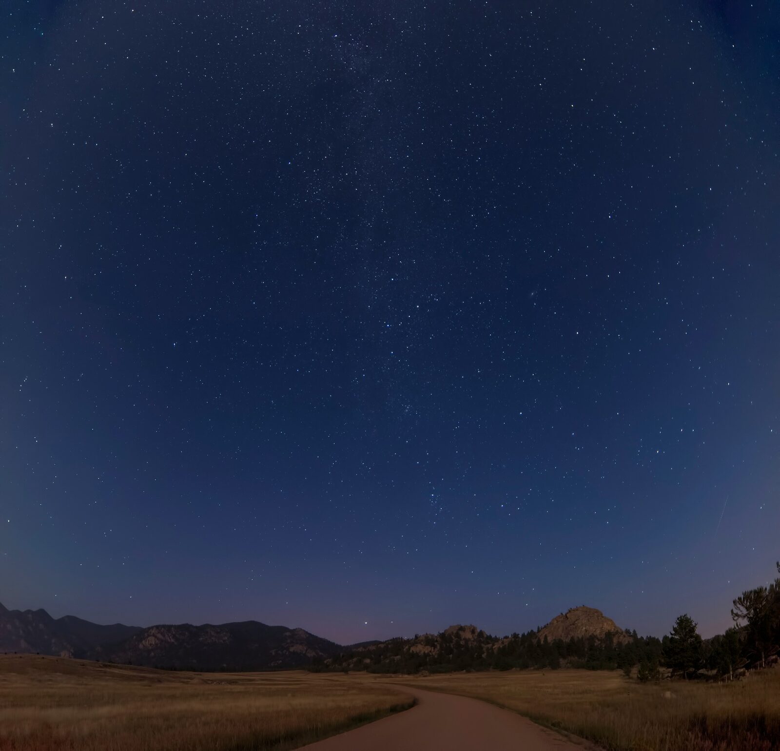 A star-filled night sky above a dark mountain road